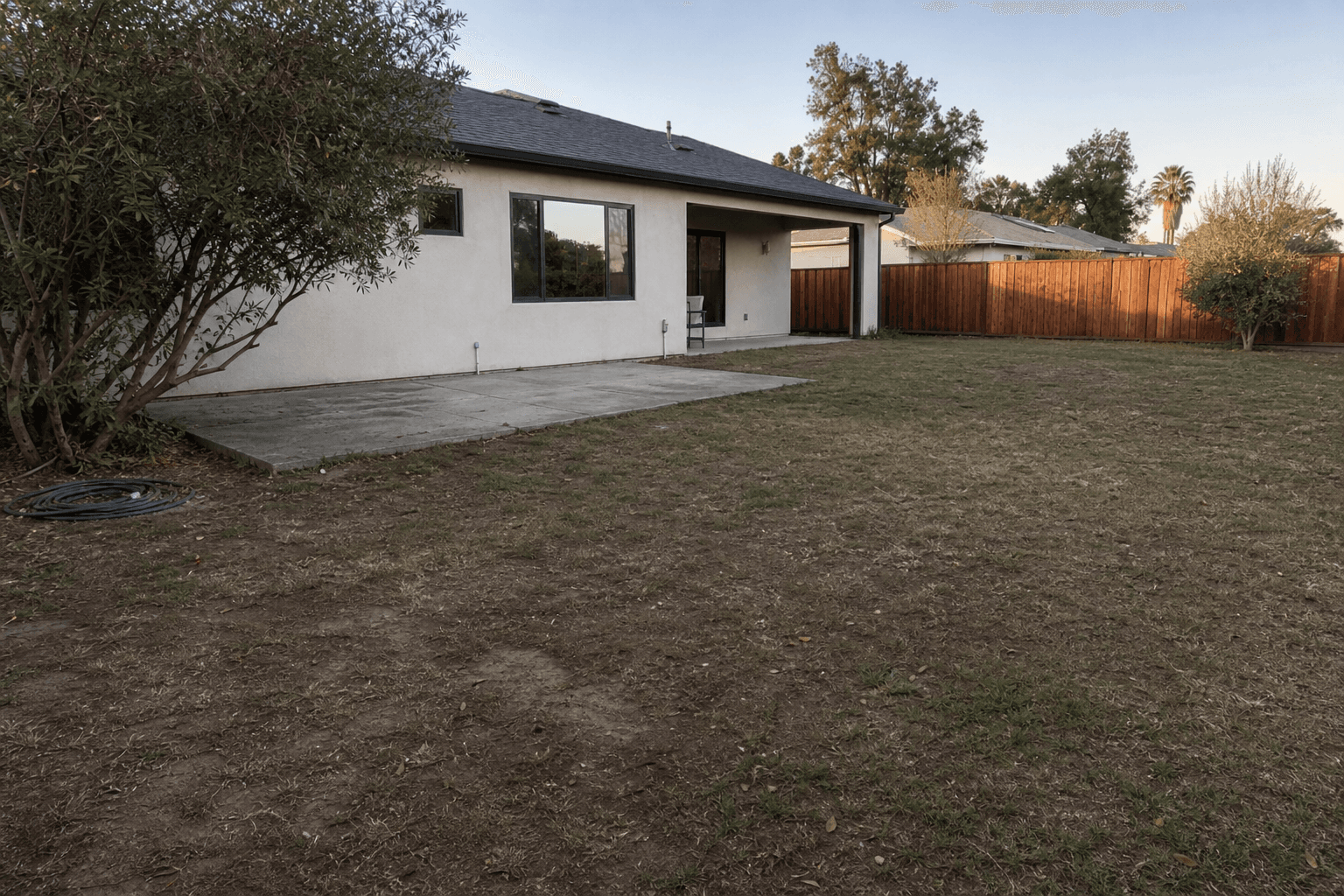 Neglected Rocklin backyard with a cracked concrete slab and patchy dead lawn before the build